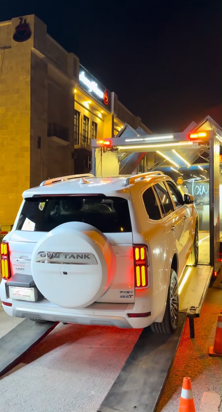 A white SUV being loaded onto an enclosed car carrier at night